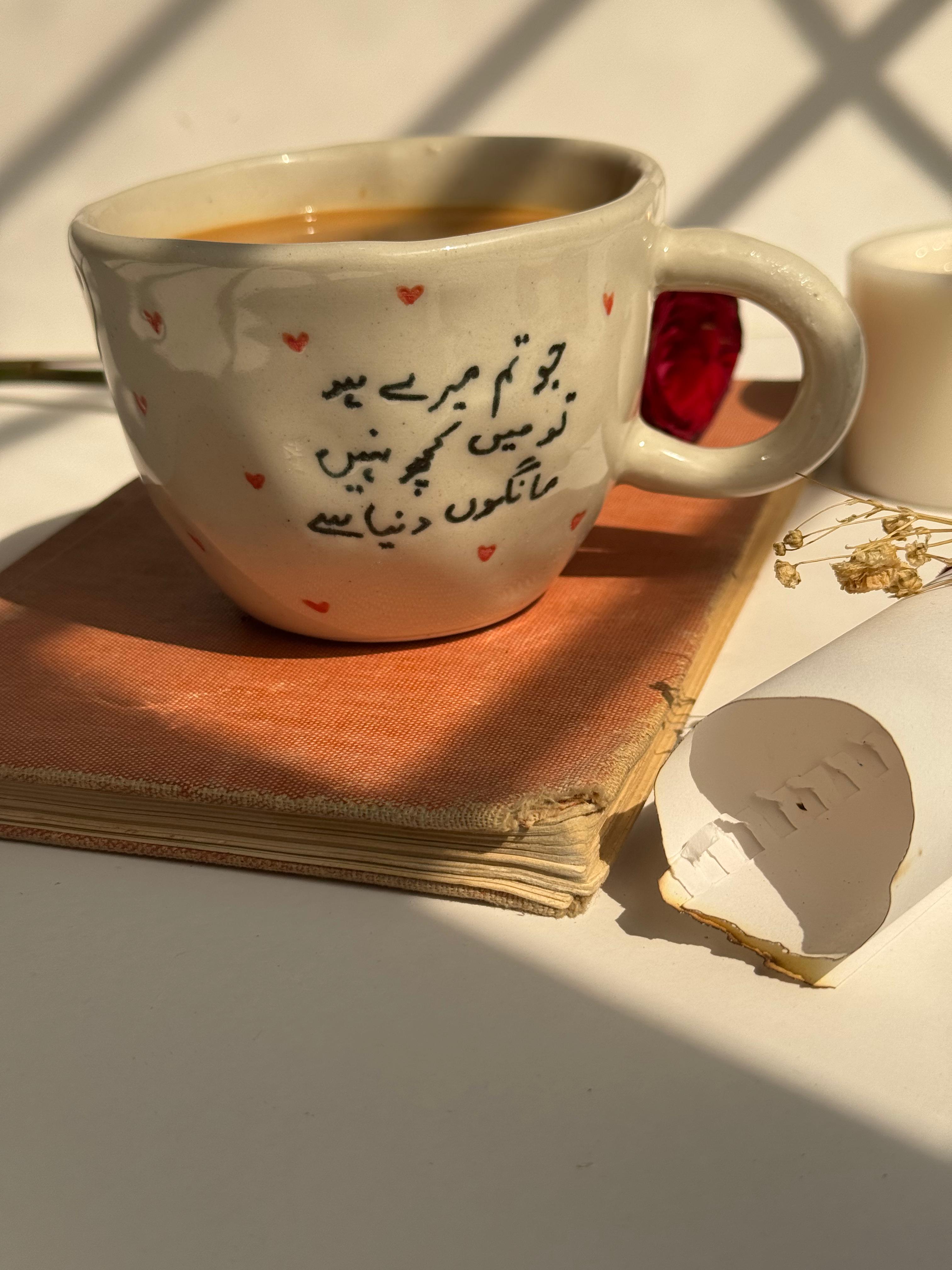 Ceramic mug with Arabic text and red hearts on a book with sunlight casting shadows