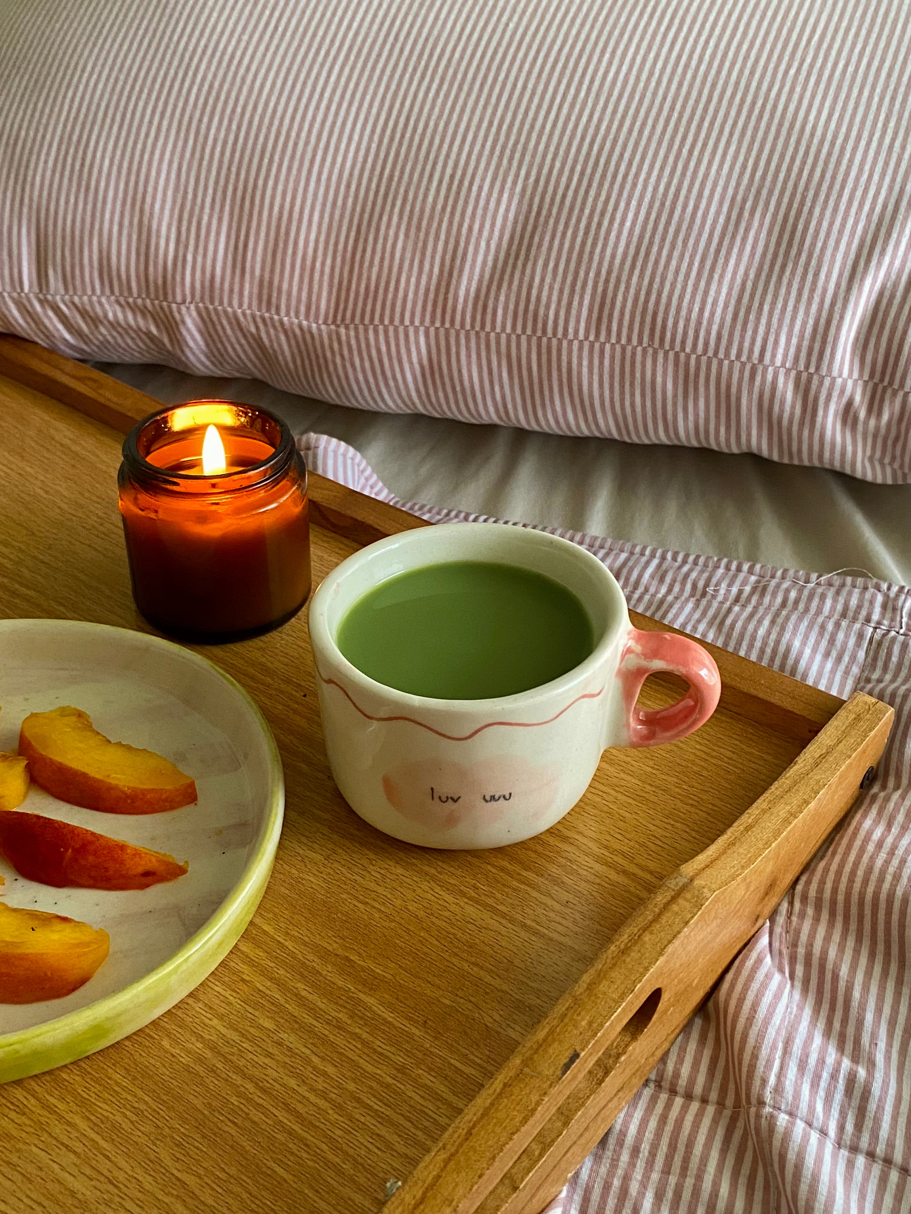 handmade ceramic macha cup wiuth love notes , gift perfect Cup of green tea macha on a wooden tray with a lit candle and peach slices, set against a striped fabric background.