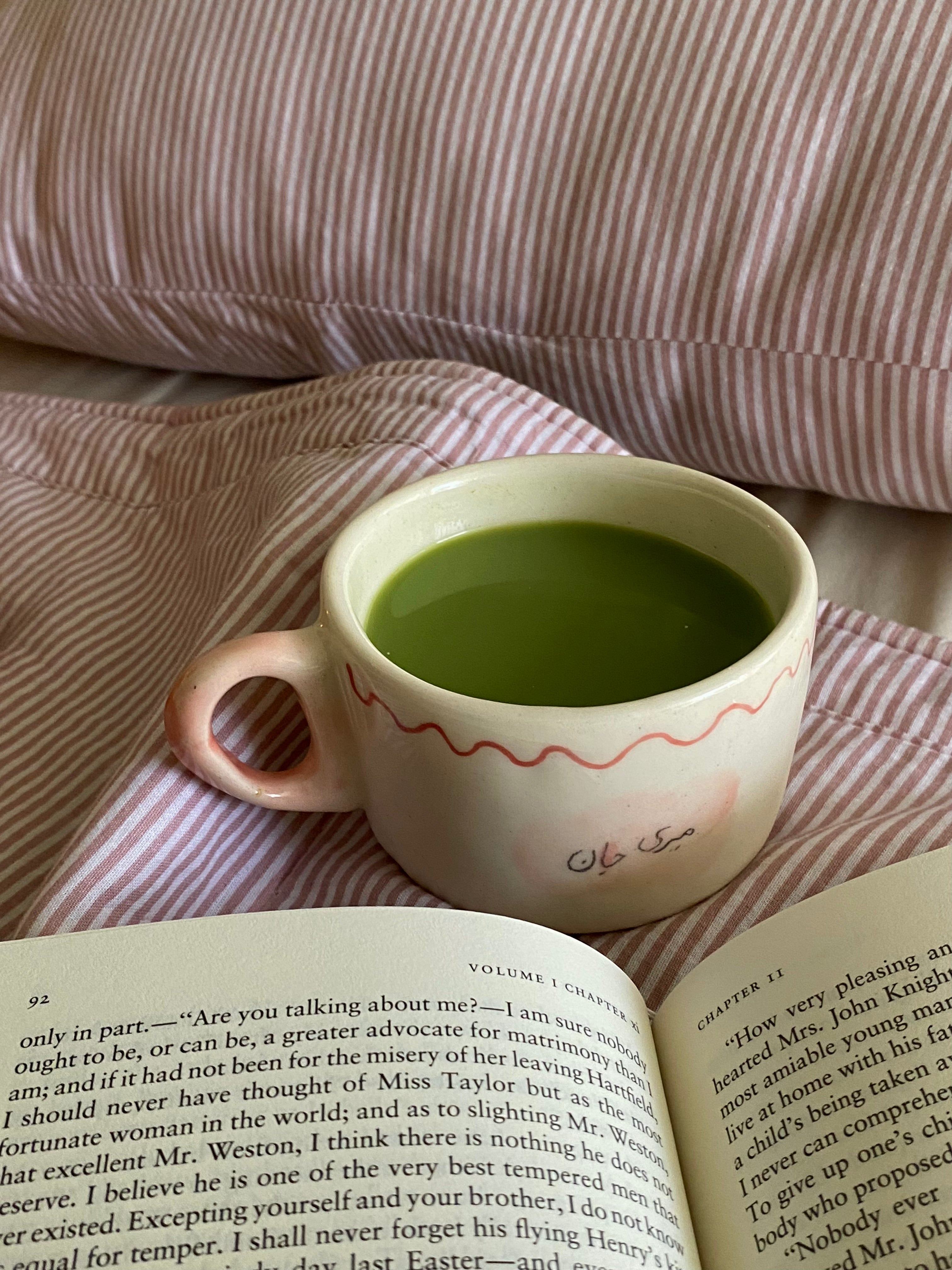 handmade ceramic macha cup wiuth love notes , gift perfect Cup of green tea macha on a wooden tray with a lit candle and peach slices, set against a striped fabric background.