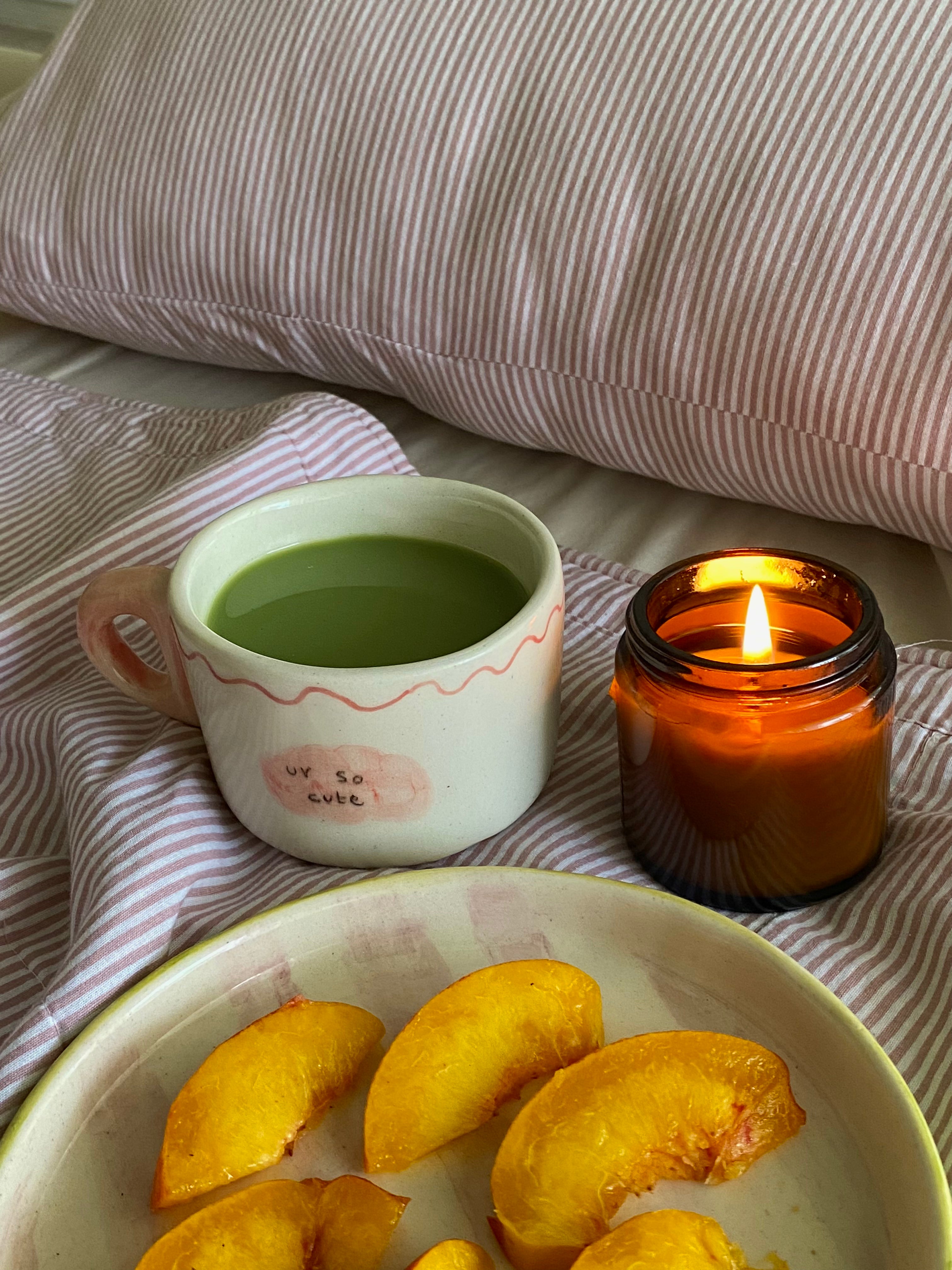 handmade ceramic macha cup wiuth love notes , gift perfect Cup of green tea macha on a wooden tray with a lit candle and peach slices, set against a striped fabric background.