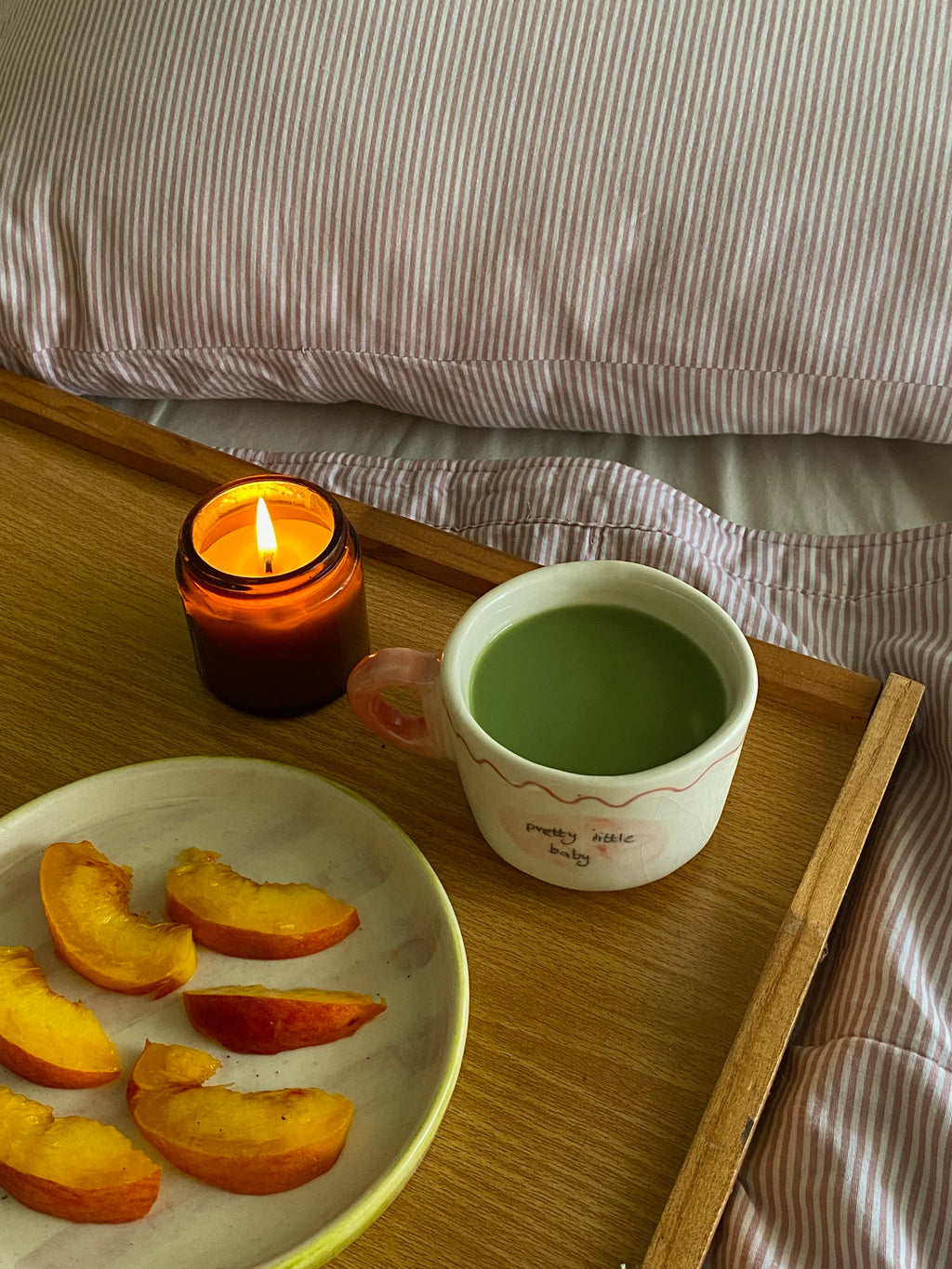 handmade ceramic macha cup wiuth love notes , gift perfect Cup of green tea macha on a wooden tray with a lit candle and peach slices, set against a striped fabric background.