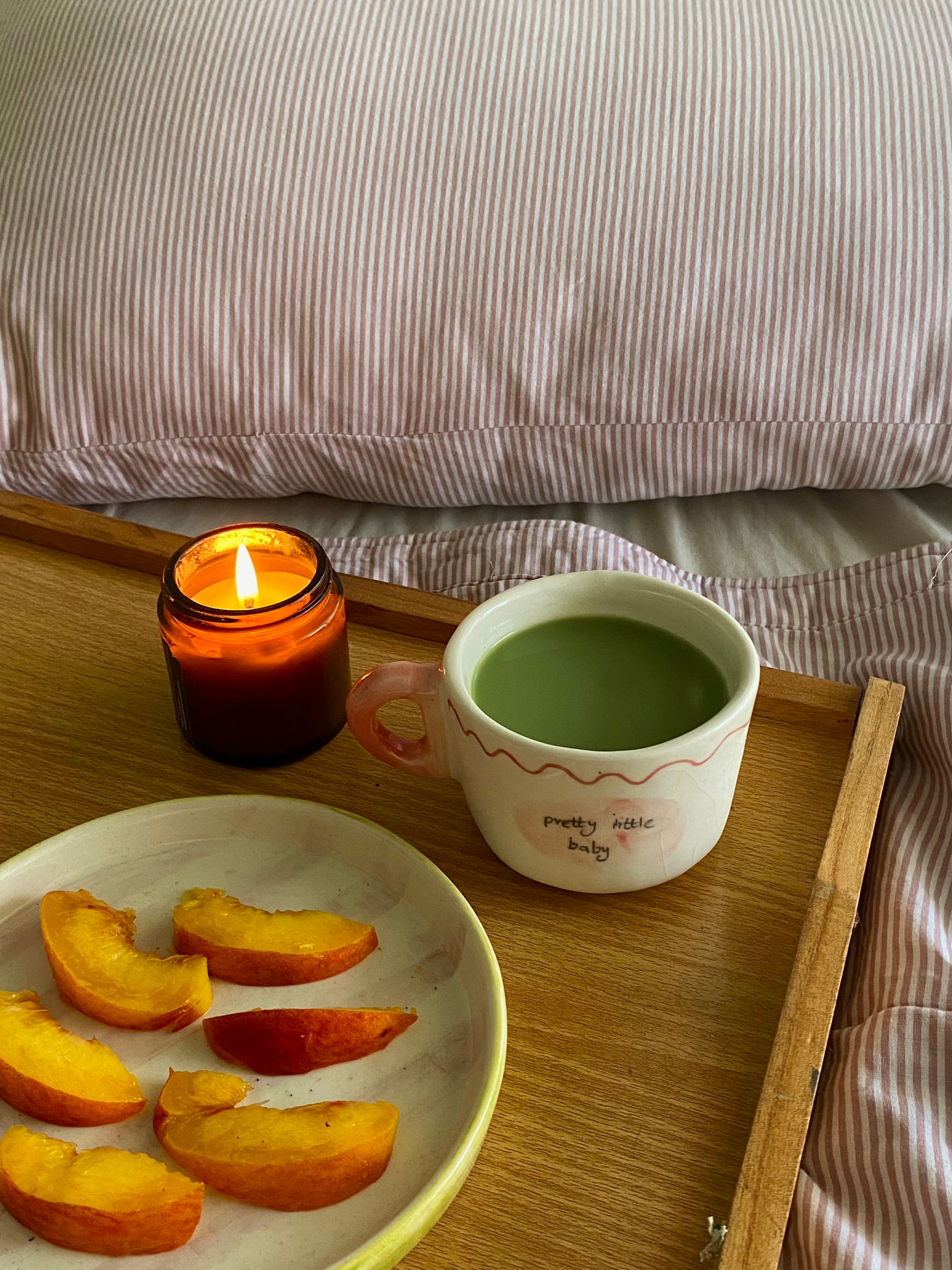 handmade ceramic mug pakistan Candle, mug, and plate of peaches on a wooden tray with striped bedding in the background