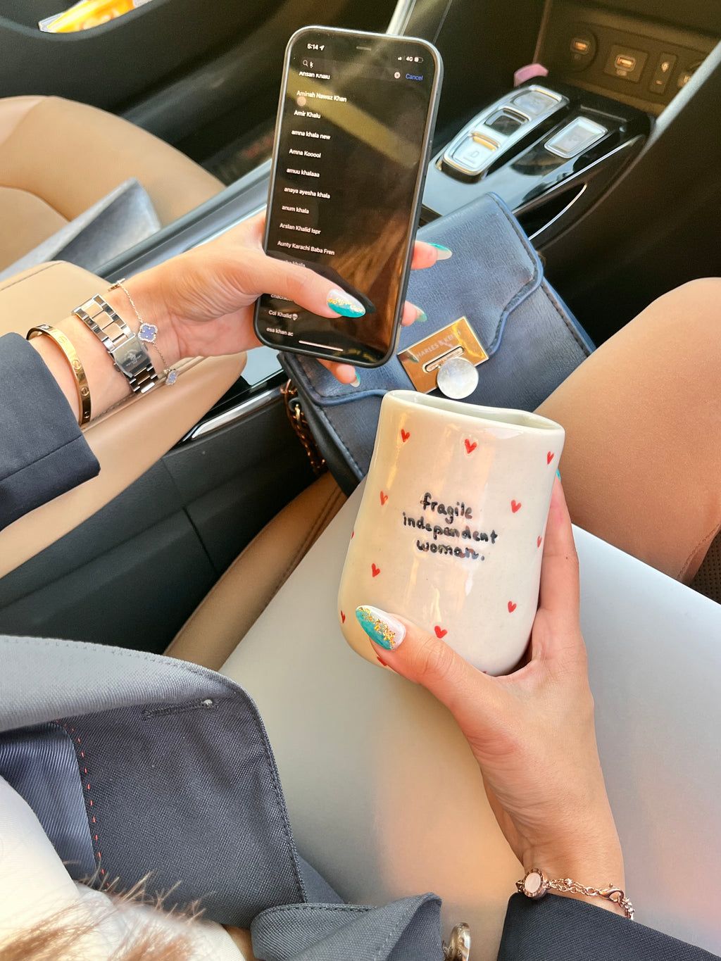 A person sitting in a vehicle holding a white tumbler with the text 'Fragile independent woman' printed on it, also holding a smartphone. handmade ceramic tumbler for iced coffee iced tea smoothies macha for girl boss entrepreneur 