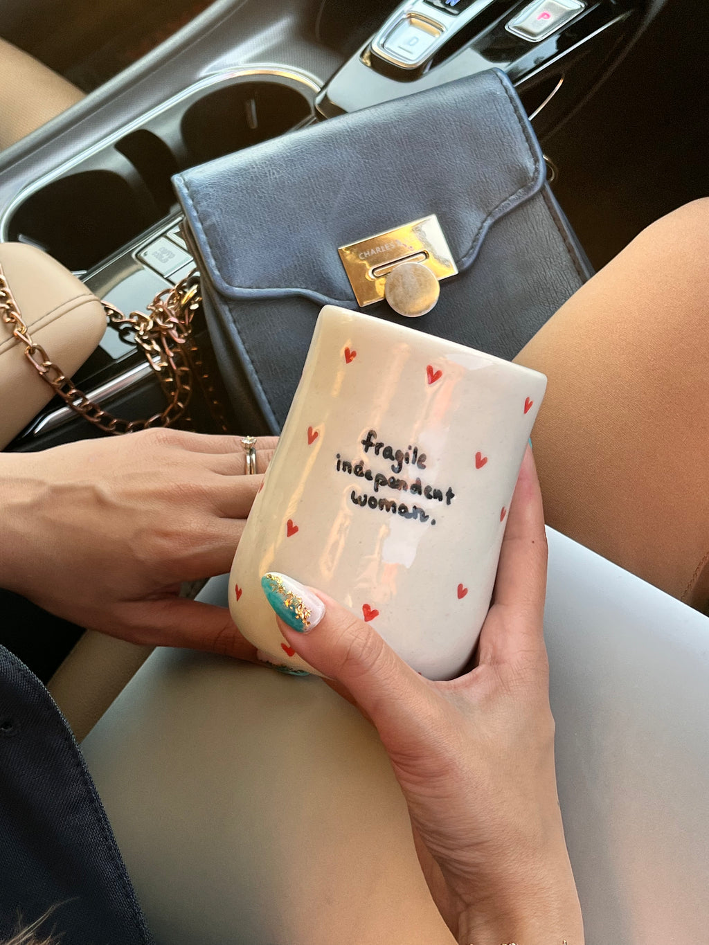 white tumbler with the text 'Fragile independent woman' printed on it, also holding a smartphone. handmade ceramic tumbler for iced coffee iced tea smoothies macha for girl boss entrepreneur 