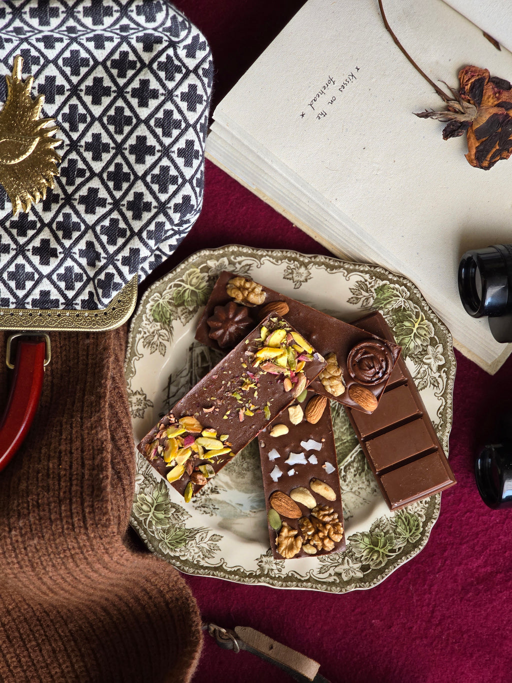 A selection of handmade chocolates with various toppings, presented on a plate next to a book and a cup of tea.