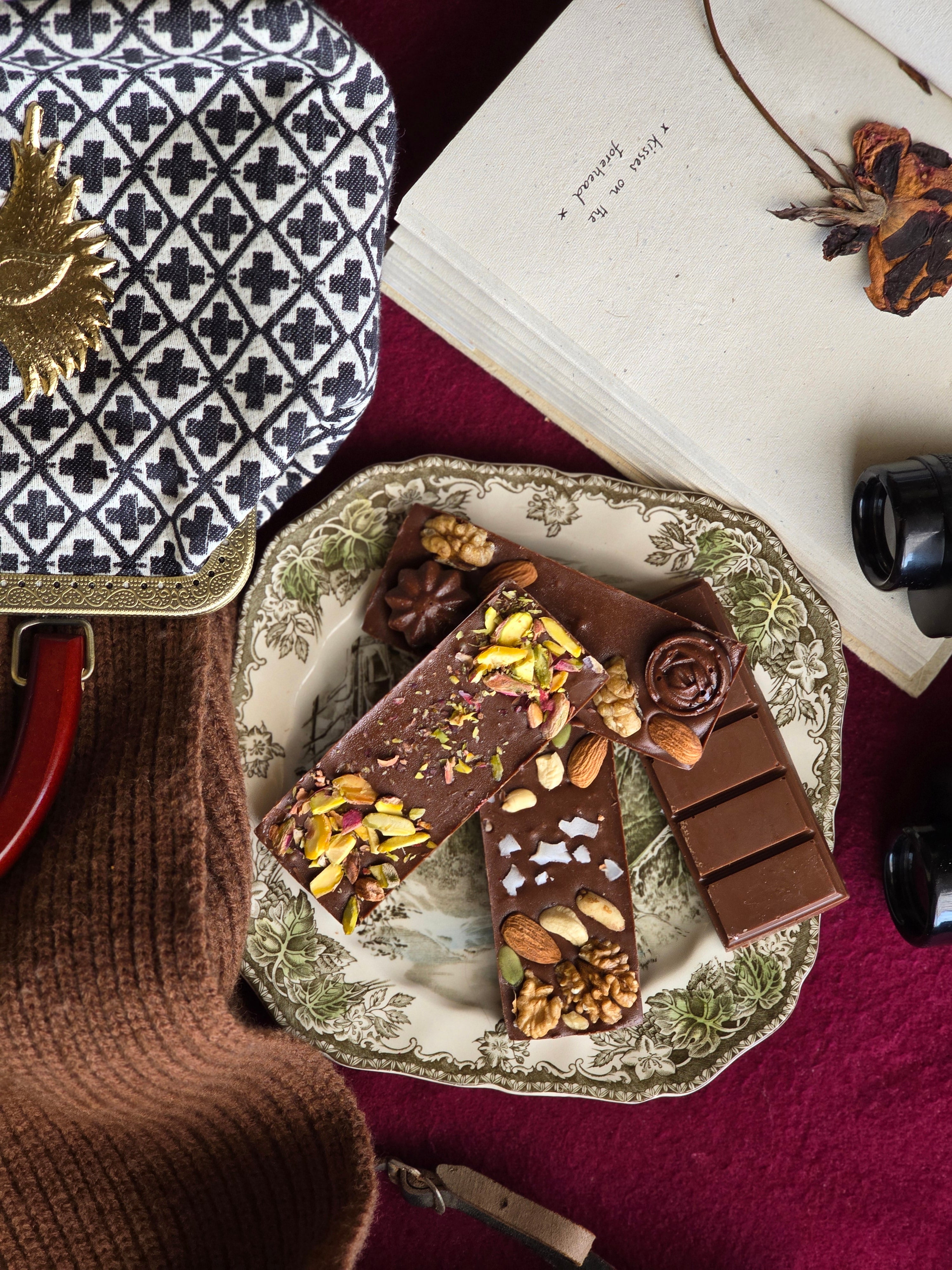 A selection of handmade chocolates with various toppings, presented on a plate next to a book and a cup of tea.