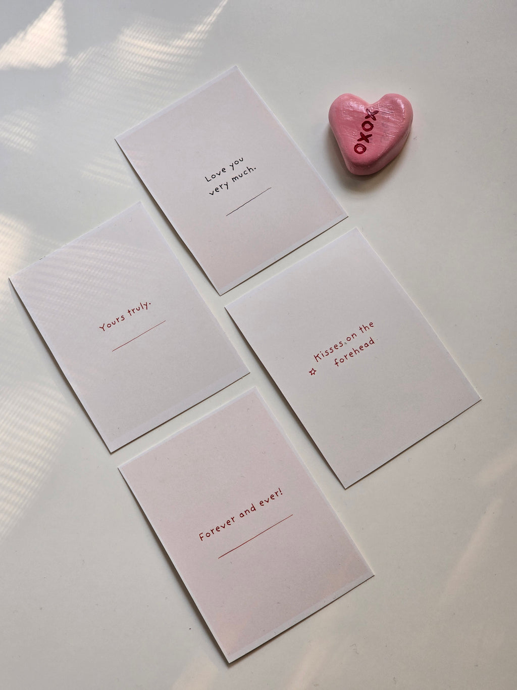 Four pink post-it notes with love messages written on them, placed on a surface with a pink heart-shaped object to the side.